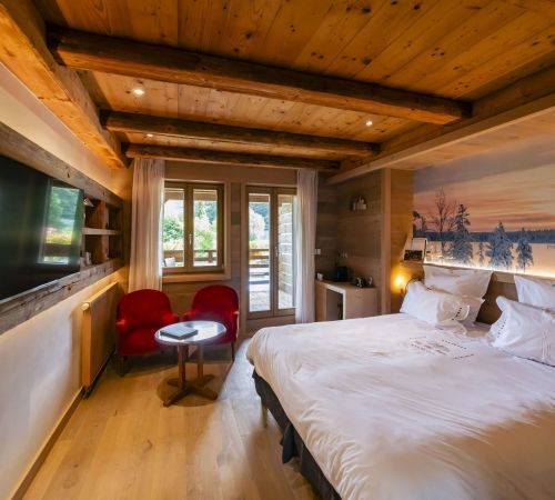 Cozy Les Bas Rupts room with winter-themed wall art, natural wood and forest-view balcony.