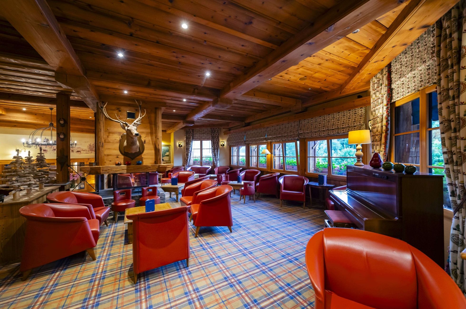 Panoramic view of the lounge bar and sitting area at Les Bas Rupts hotel, with wood decor and red armchairs.